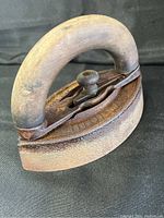 Side angle view of the iron showing wooden handle and cast iron body with surface wear and patina.