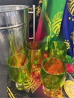Photo showing two metal champagne buckets, four green plastic wine glasses, the beach pareo fabric, and part of the wine decanter