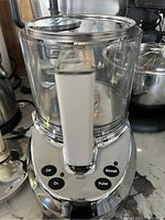 Photo of the food processor motor base and attached clear bowl. Buttons for Off, On, Dough, and Pulse are visible on the base.