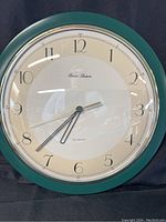 Front view of the Daniel Dakota wall clock showing the green trim, clock face with numerals, and clock hands.