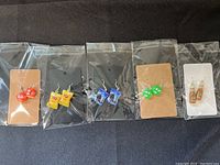 All five pairs of novelty earrings displayed in packaging: red M&M's, yellow Lay's chips bag, blue Oreo cookie bag, green M&M's, and Starbucks bottled iced coffee drink.