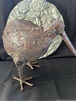 Close-up side view of cast iron bird sculpture with round floral garden stone in background
