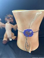 Photo showing the ceramic trash can shaped like a rolled parchment with a blue 'Hp' seal and a silver cord, alongside the Timon plush toy.