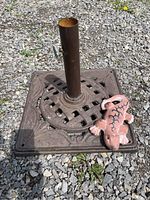 Full view of the heavy cast iron umbrella base sitting on gravel with the terra cotta iguana placed on it.