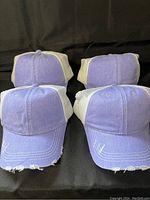 Four lilac distressed baseball hats, showing front and back detail, highlighting mesh back and worn edges