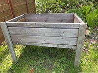 View of large raised garden bed made of wood, untreated, weathered, sturdy rectangular box on four legs.