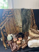 Five animal print scarves displayed on a dark background along with a pillow sham, black mug, three covered candles, and scent warmer with wax melts