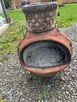 Front view showing wide fire opening filled with ash residue, terracotta body and black iron loops on sides.