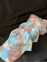Four ponytail hats displayed in a line, two with blue tie-dye and two with pink tie-dye colors, showing their distressed cotton fabric and bill shape.