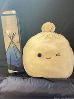 Photo showing the unopened box of Pep Step Teepee play tent standing upright next to the large Squishmallow plush