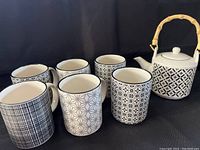Seven-piece set with a white Stokes teapot and six Casa Moderna mugs, all decorated in black geometric designs.