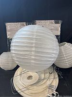 Two black packaged microfiber tablecloths shown behind white round paper lanterns and metal wire frames.