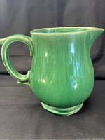 Green McCoy pottery pitcher with curved handle and spout, showing surface crazing typical of vintage condition.