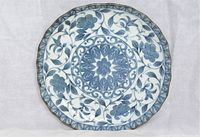 Full view of one blue and white porcelain plate with floral pattern and scalloped edge.