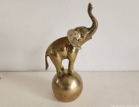 Side angle showing the brass elephant figurine standing on a brass sphere with trunk raised