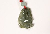 Front close-up view of green jade horse pendant with bead and red cord.