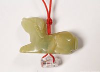 Front angle of light green carved dog pendant on red cord with clear bead