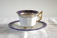 Side view of demitasse cup on saucer showing golden handle and blue and gold designs.