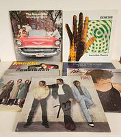 Five classic rock vinyl LP records shown, featuring The Guess Who, Genesis, Foreigner, Huey Lewis & The News, and Peter Frampton album covers.