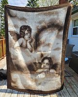 Full front view of blanket showing two cherubs and cloudy sky design with brown border.
