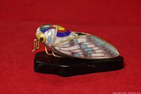 Side view of the enameled brass cloisonné cicada figurine showing detailed wing patterns and wood base.