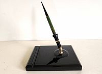 Green and black Parker pen with gold accents positioned vertically on a glossy black square stand with circular holder.