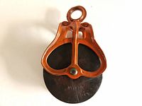 Top view of the refurbished barn pulley showing the orange metal frame and wooden wheel.