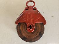 Front view of red cast iron barn pulley with circular hook and metal pulley wheel showing rust and wear.