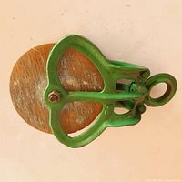 Top view of the refurbished barn pulley showing green metal frame and wooden wheel