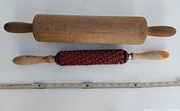 Two rolling pins, one wooden and one embossed, with a ruler below for scale showing approximately 18-19 inches in length each