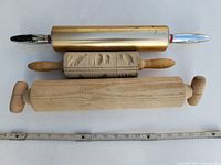 Photo showing 3 vintage rolling pins arranged horizontally with measuring tape below for scale.