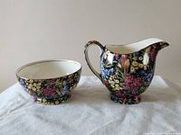 Front side of the creamer and sugar bowl displaying floral chintz pattern with black background.