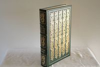 Front cover of green leather-bound hardcover book with elaborate vertical gold embossed leafy design on the front