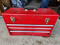 Closed red tool box showing two metal latches, carrying handle, and signs of wear and rust