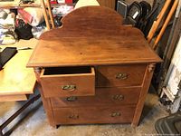 Front view showing wash stand with four drawers, two smaller top drawers and two larger bottom drawers, all with brass handles. The wood has a warm brown stain with visible wear and a decorative shaped backsplash.