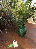 Green ceramic vase holding artificial fern-like leafy plant, photo shows size and detail of item.