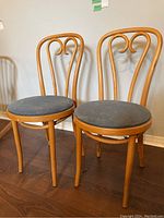 Two bentwood Thonet style cafe chairs with beige wooden curved frames and dark grey round cloth seats, shown from frontangle