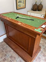 Side view showing the wooden bar structure with paneled sides, green felt blackjack game board top with card layout markings, and wooden grooves and cup holders around edges.