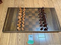 Full top down view of the rectangular wooden chess board with all light and dark wooden chess pieces placed along the sides.