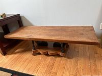 Front angle view of the rectangular wooden coffee table showing the worn tabletop and distinctive wooden base with turned legs.