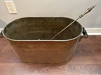 Copper bin viewed from side angle showing size and shape with poker resting inside.