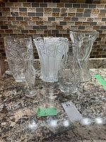 Five crystal pieces grouped together on countertop showing pinwheel vases, water jug, and cut glass vase.