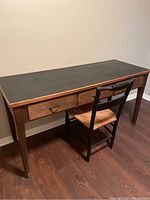Full view of wood desk with black leather inlay on top and accompanying wooden chair with rush seat.