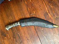 Kukri dagger sheathed showing the black sheath with brass tip and dark handle with metal and decorative inlays.