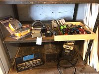 Wide view showing the wet stone sharpener at the bottom shelf with various hand tools on the upper shelf including screwdrivers, clamps, and socket set.