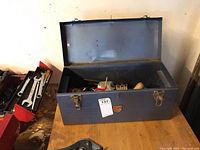 Blue metal tool box open on a wood table, showing interior and dents on the box exterior