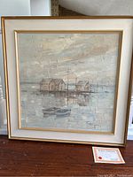 Full view of the framed oil painting of houses on stilts over water with boats and cloudy sky, showing style and size, with certificate visible on floor.