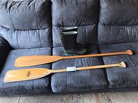 Two wooden canoe paddles and a pair of rain boots arranged on a gray couch, showing overall items in the lot.