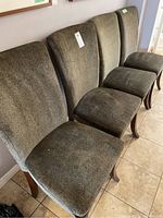Four Ashley Furniture Parson dining chairs in dark olive green upholstery, seated in a row against a wall showing front and top surfaces of chairs.