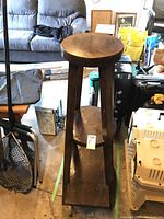 Front view of the tall wooden plant stand showing the round top shelf, middle shelf, and triangular bottom shelf.